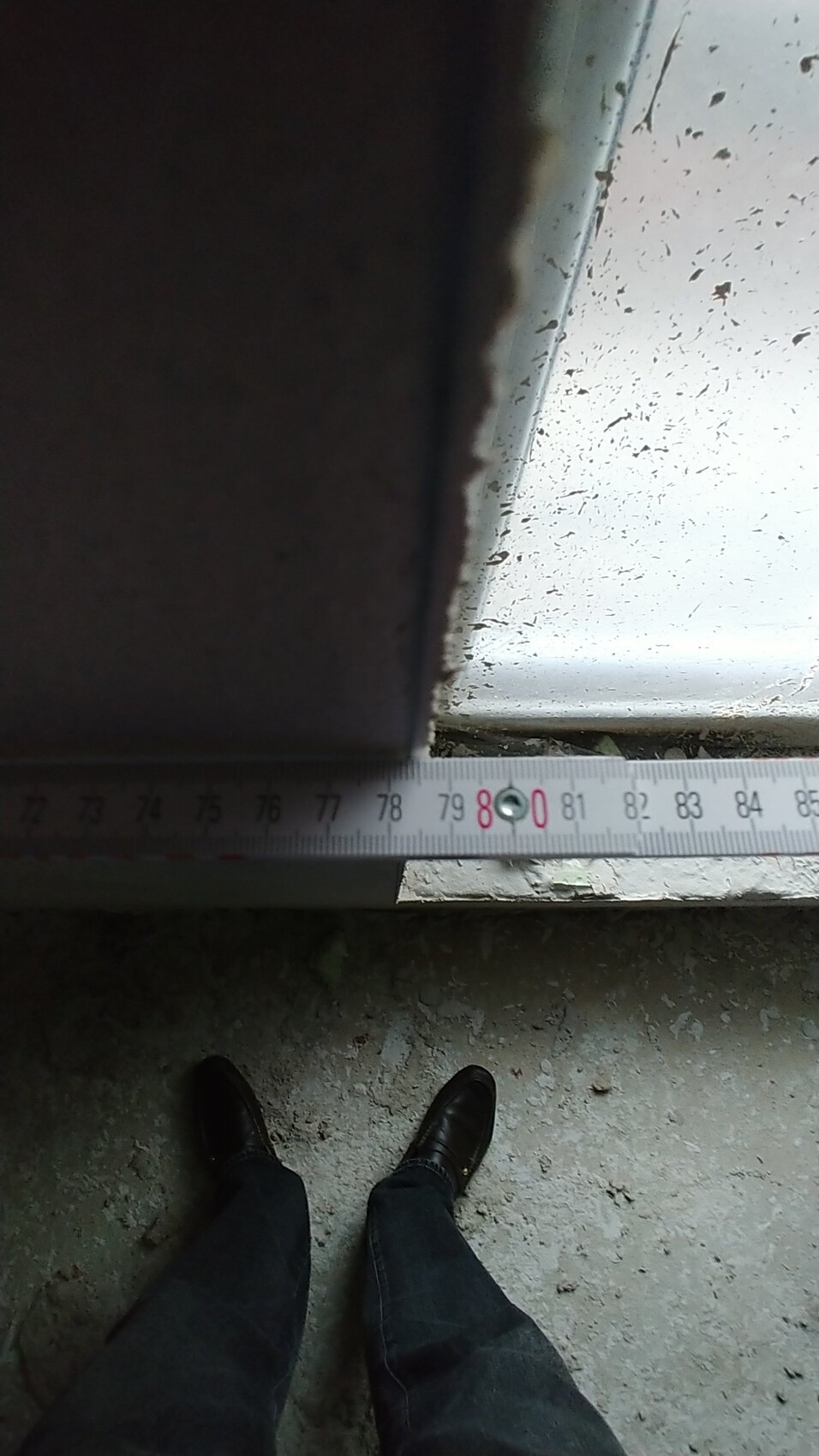Person steht auf einer Baustelle vor Türschwelle; Maßband zeigt ca. 80 cm, Boden uneben.