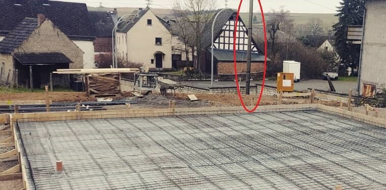 Baustelle mit Fundamentplatte und Stahlarmierung; Hintergrund Häuser; roter Kreis markiert orangefarbenes Baugerät.