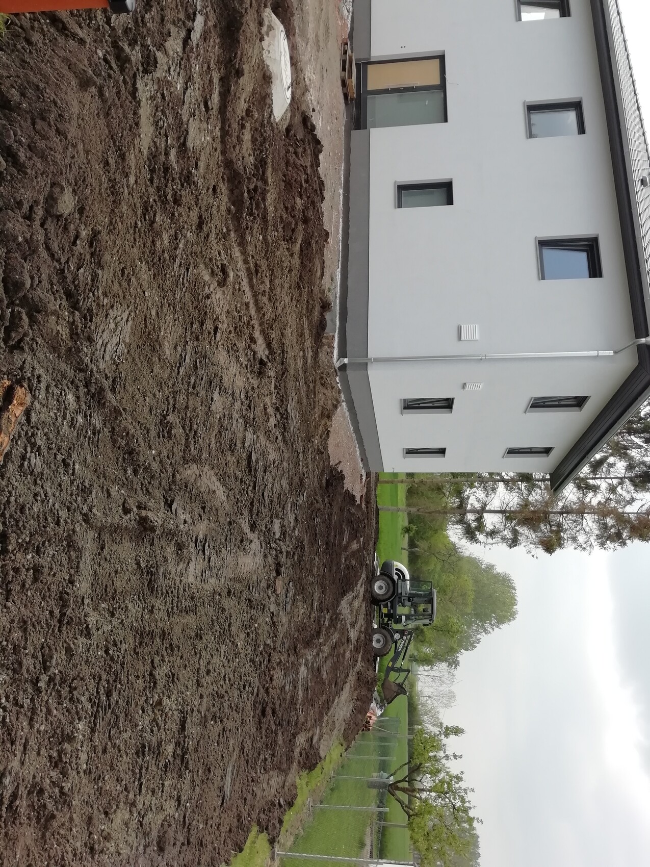 Baustelle mit Erdaushub neben weißem Haus und Baufahrzeug im Hof.