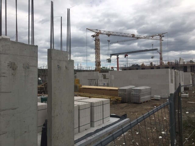 Baustelle mit Betonstützen, Paletten, Kran im Hintergrund und Baumaterialien im Vordergrund