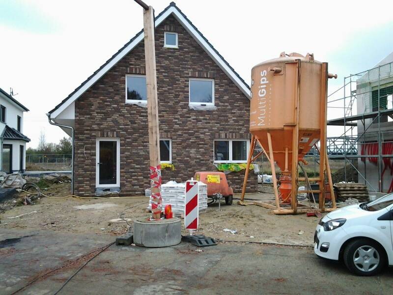 Neues Haus im Rohbau mit Backsteinfassade, Baumaschinen und Bauzubehör auf Baustelle