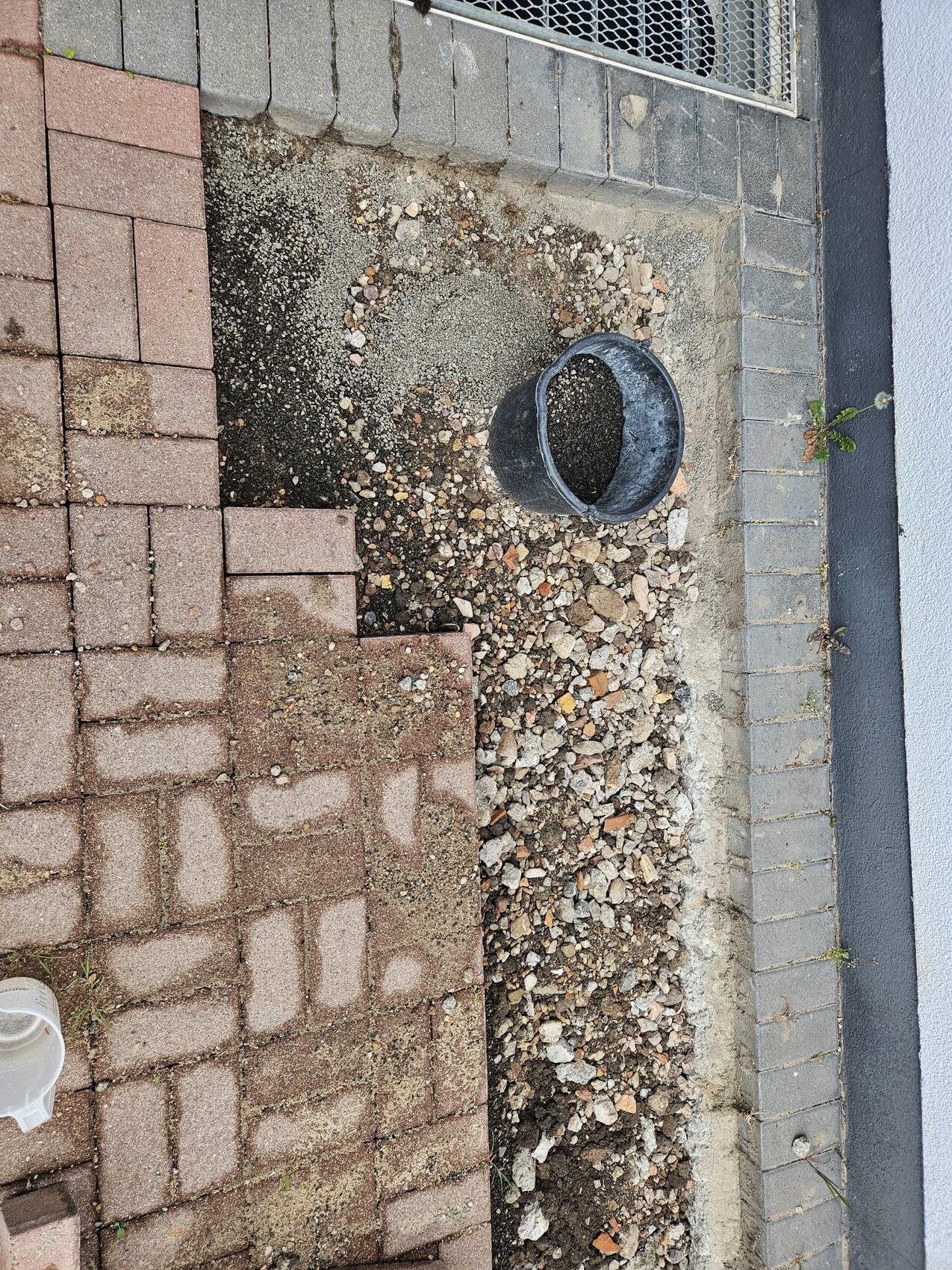 Außenbereich mit Pflastersteinen, Kies und einer Grube neben der Hauswand.