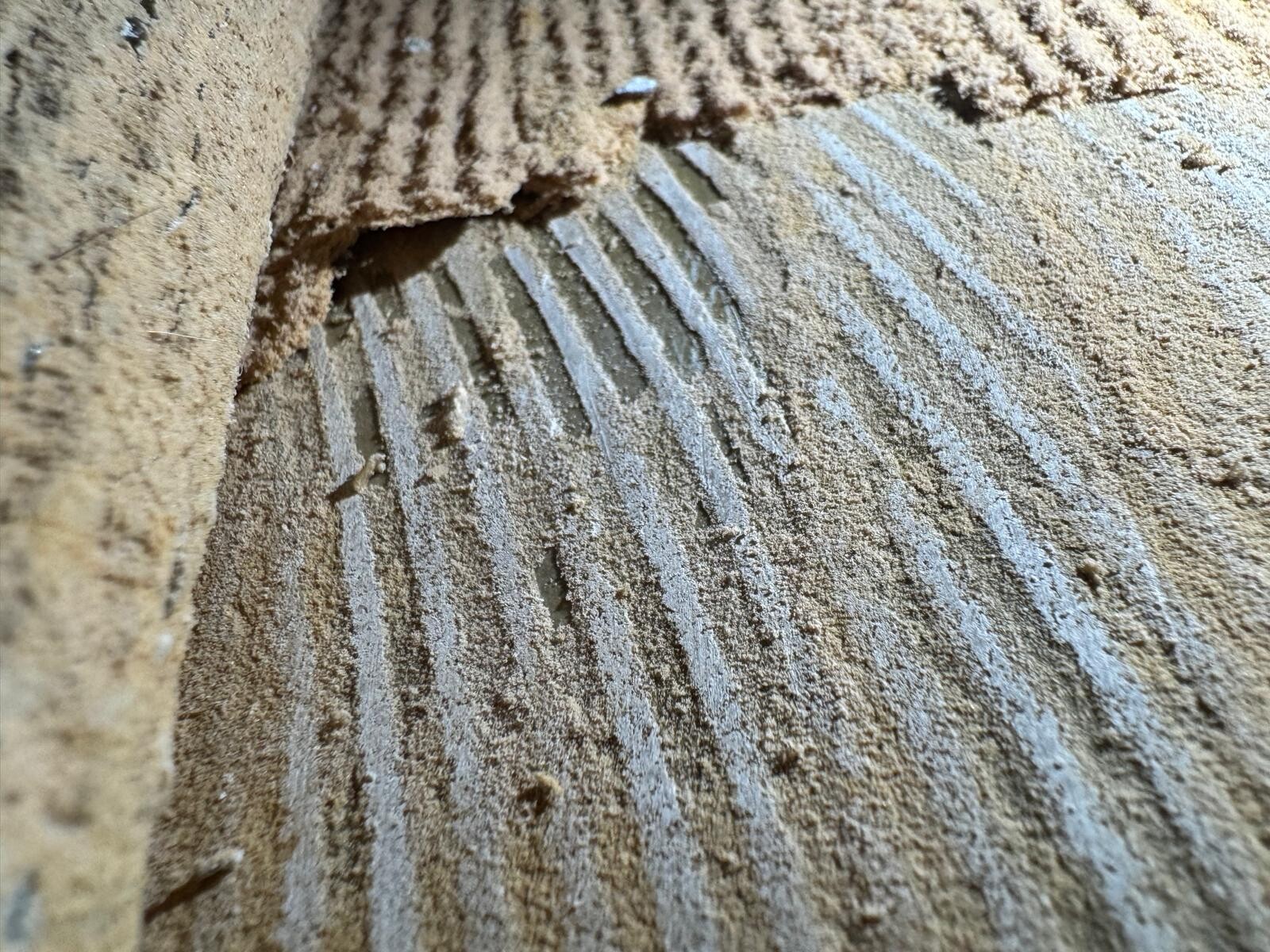 Nahaufnahme einer sandigen Oberfläche mit parallelen Rippen und feinem Staub.