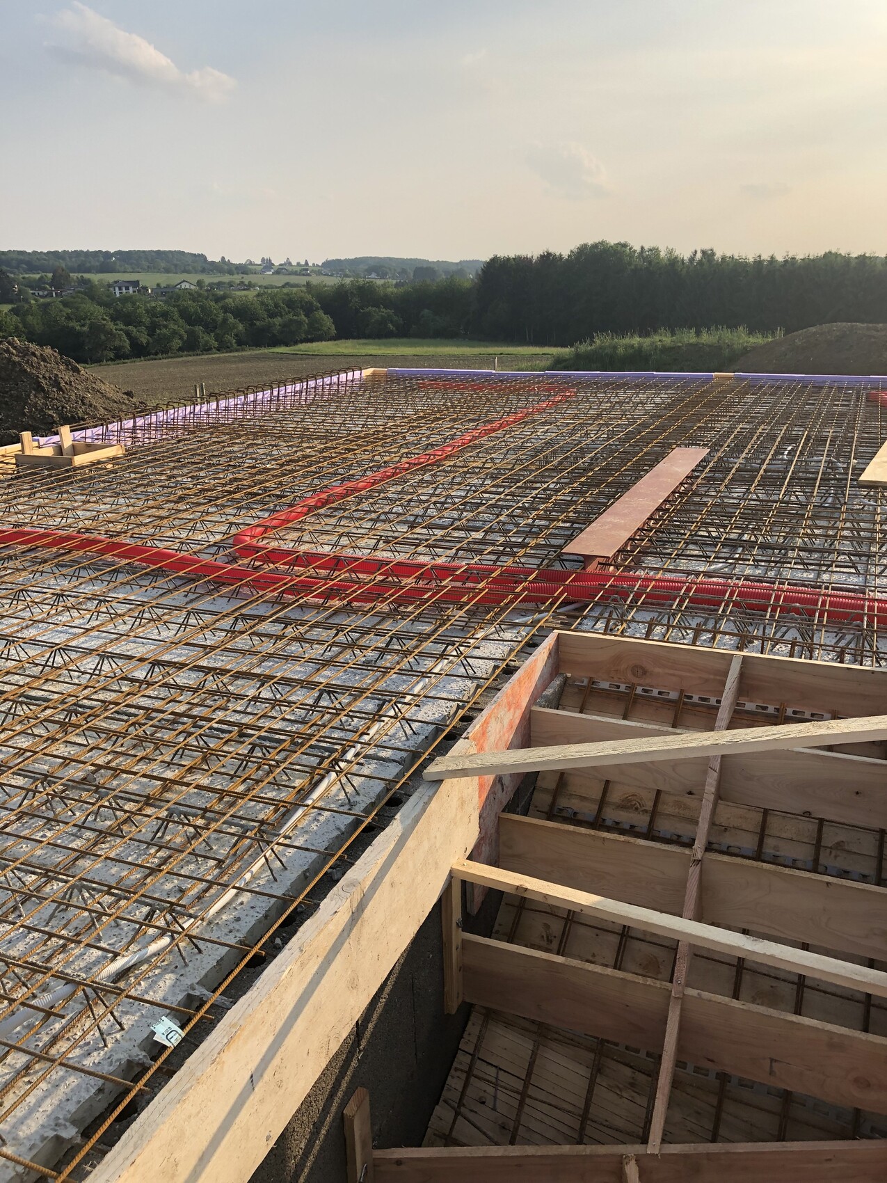 Bewehrungsstahlnetz auf Gussdecke rote Leitungen, Holz-Schalung; ländliche Landschaft im Hintergrund.