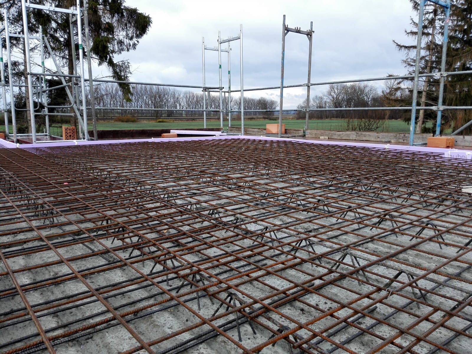 Bewehrungsstahlnetz liegt über einer Betonplatte auf einer Baustelle mit Gerüst.