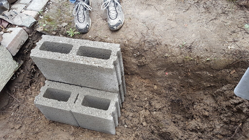 Baustelle mit Betonblocksteinen auf Erdreich; Bauschuhe im Vordergrund