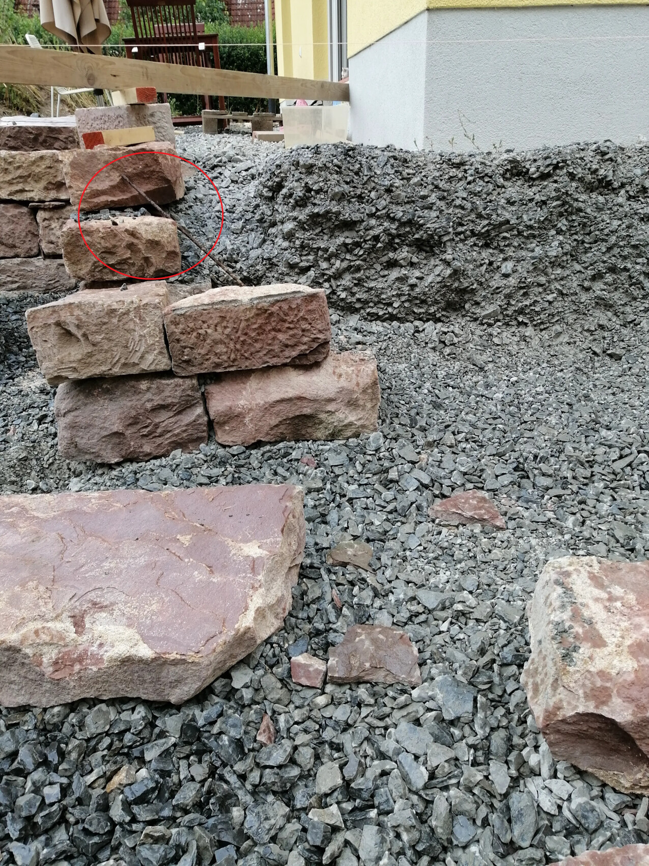 Baustelle im Garten: Unregelmäßig gestapelte rotsandsteine auf Kies, Hauswand im Hintergrund.