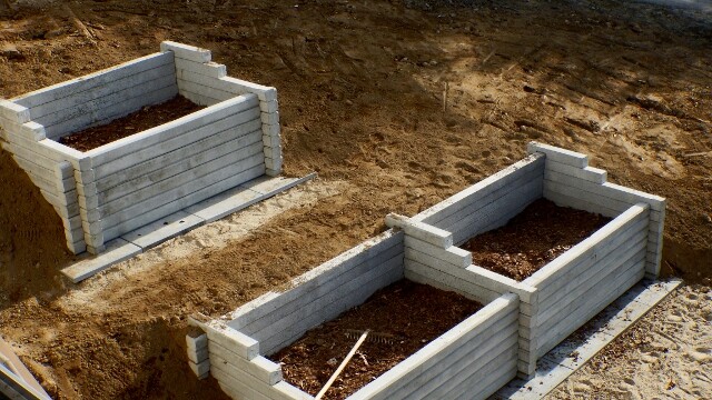 Mehrere Betonsteinmauern bilden Rohbau-Grundmauern in einer Baugrube.