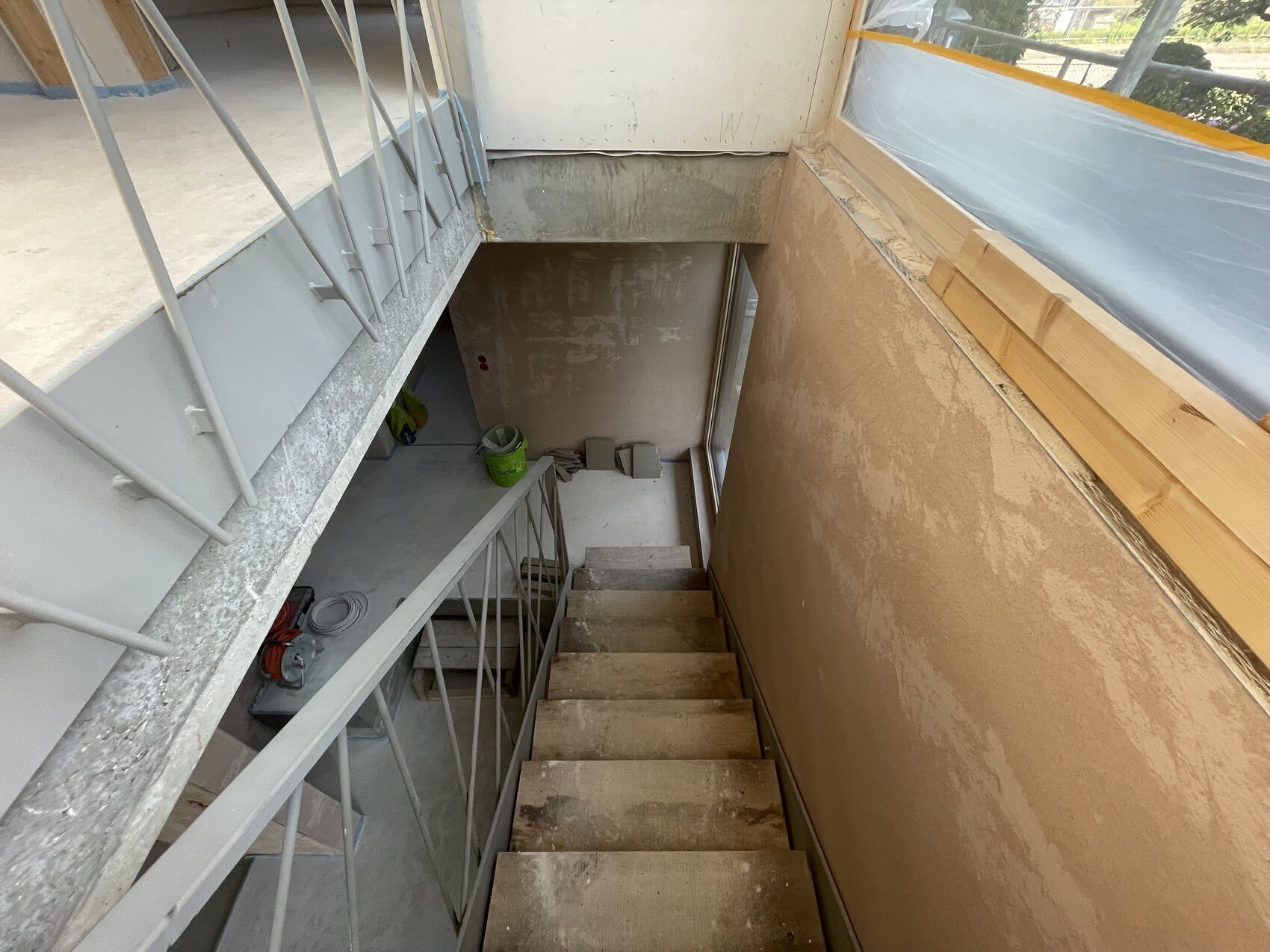 Blick von oben auf eine Baustellen-Treppe nach unten, Stahlgeländer, unfertige Wände.