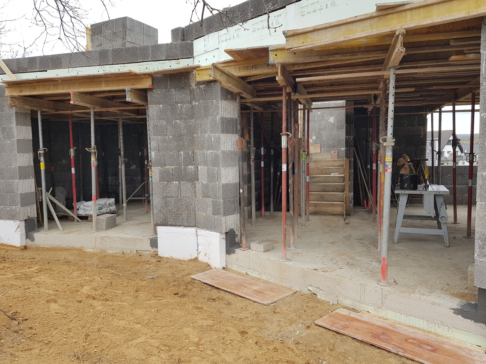 Rohbau eines Gebäudes mit Betonsteinwänden, Stützgerüsten, Holzformen und Bauwerkzeugen.