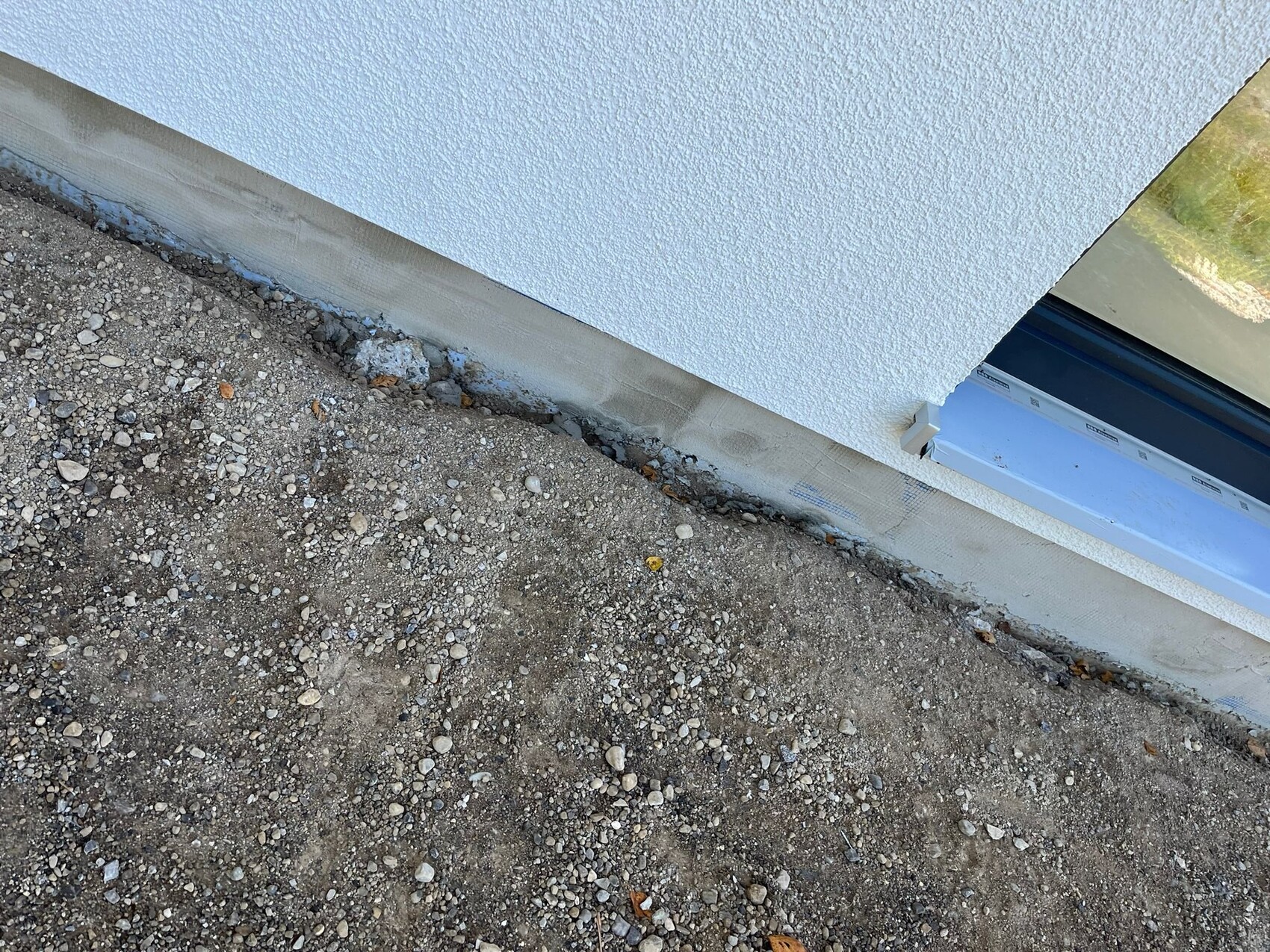 Weiße, strukturierte Außenwand über Kiesboden; unten Betonfundament, rechts Fensterbank