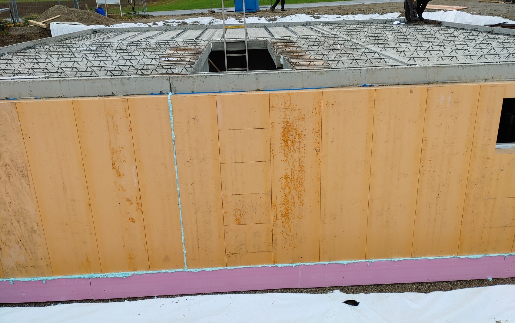 Baustelle: Betonboden mit Bewehrung, Loch im Betonboden, Holzformwände, Bauarbeiter im Hintergrund