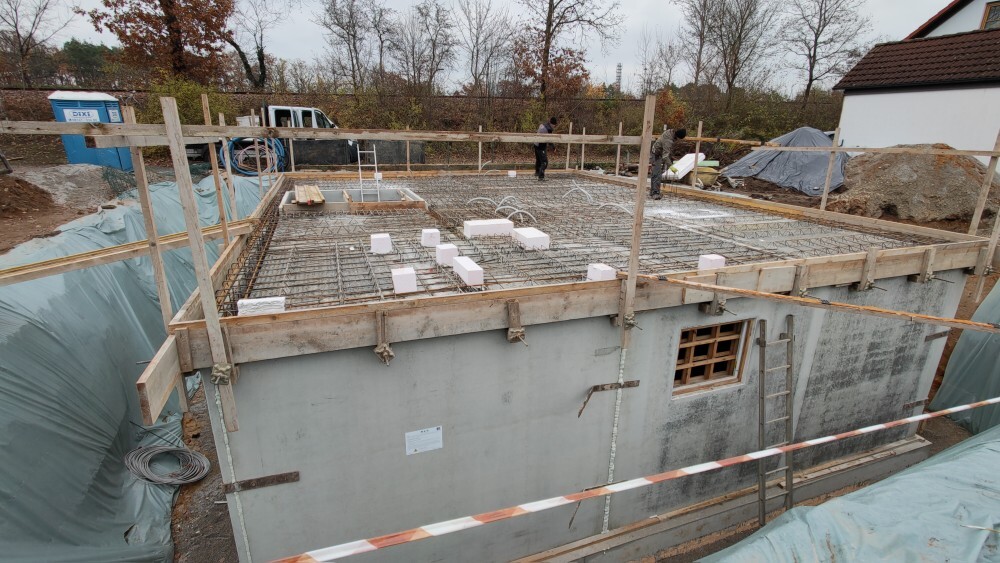 Fundament aus Beton mit Bewehrung, Holzrahmen und Blöcken, Bauarbeiter im Hintergrund