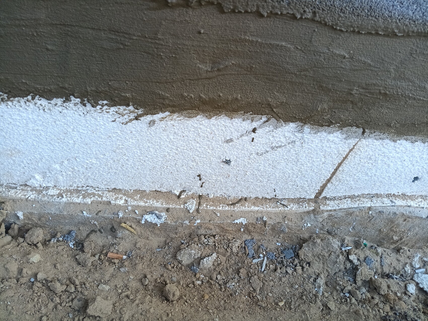 Fundamentwand aus Beton mit weißer Isolationsschicht und erdigem Untergrund.