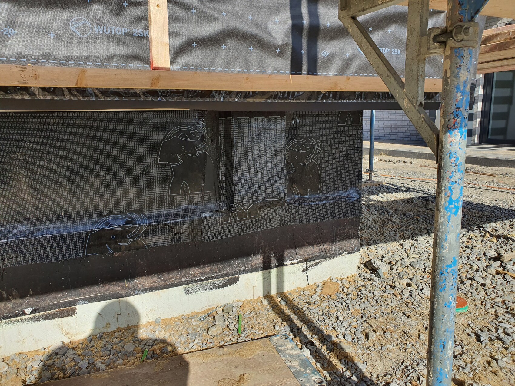 Baustelle: schwarze Dichtbahn mit Elefanten-Motiven, Gerüst und Kiesboden