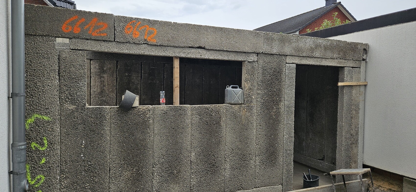 Graue Betonwand mit zwei Öffnungen; In den Öffnungen liegen Kanister, Wasserflasche und Werkzeug.
