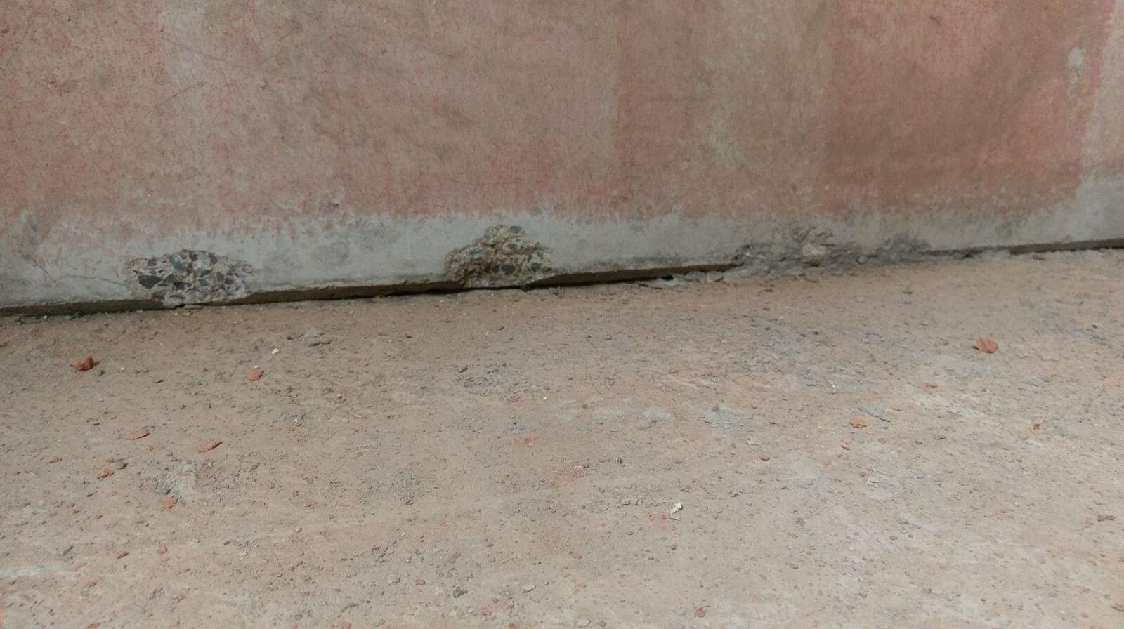 Unterkante einer rohen Wand mit beschädigtem Fundament und staubigem Erdreich