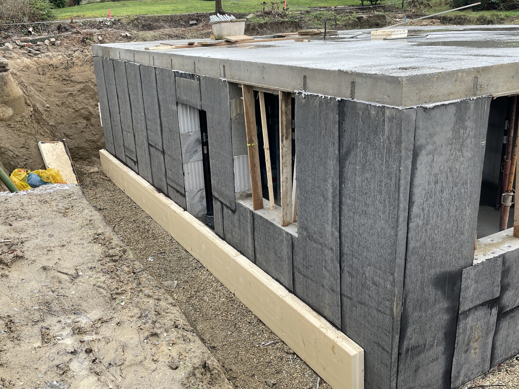 Baugrube mit grauen Betonblockwänden und Fensteröffnung im Rohbau.