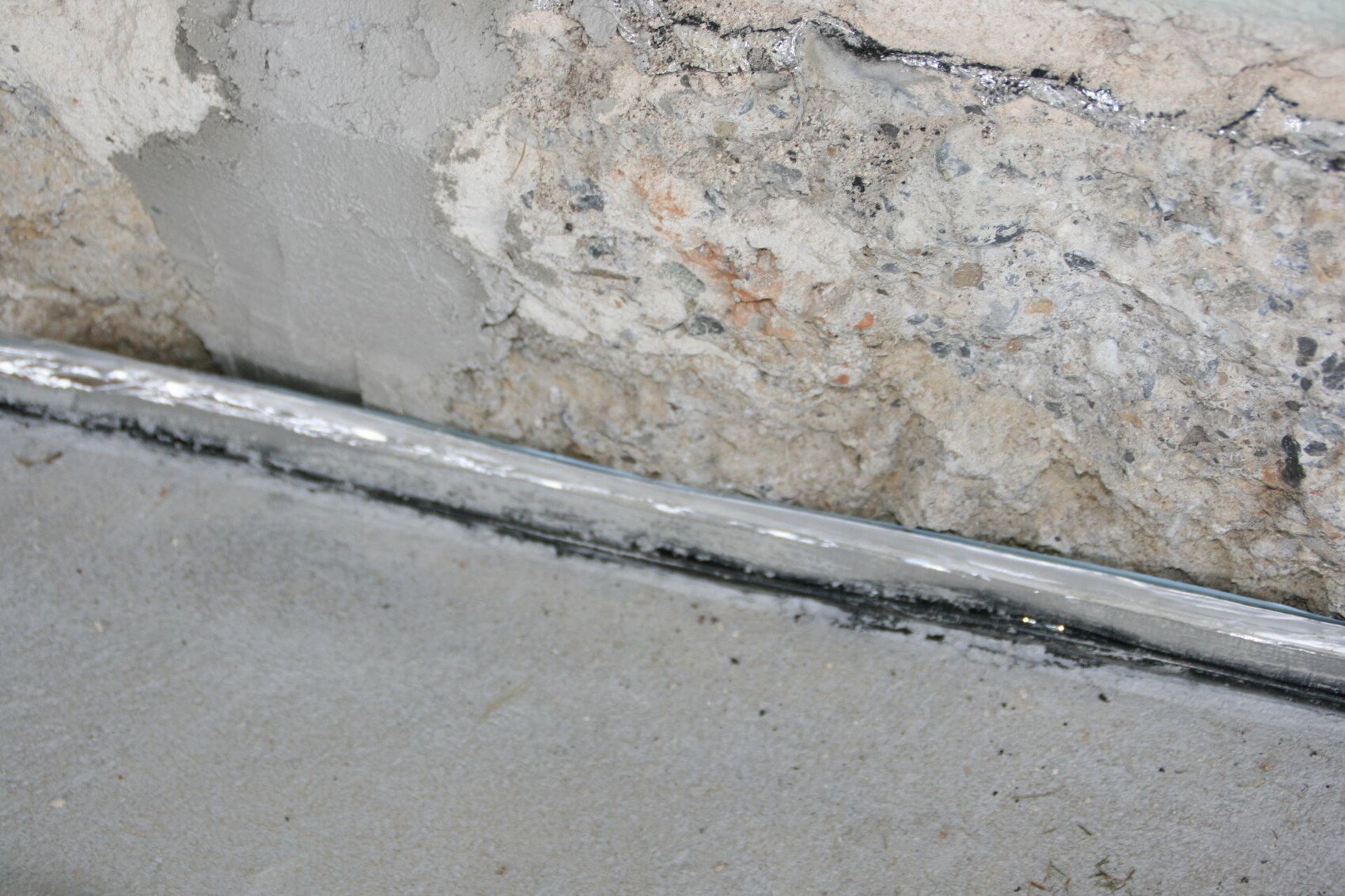 Raues Betonfundament und Wand mit Putzresten am Bodenbereich