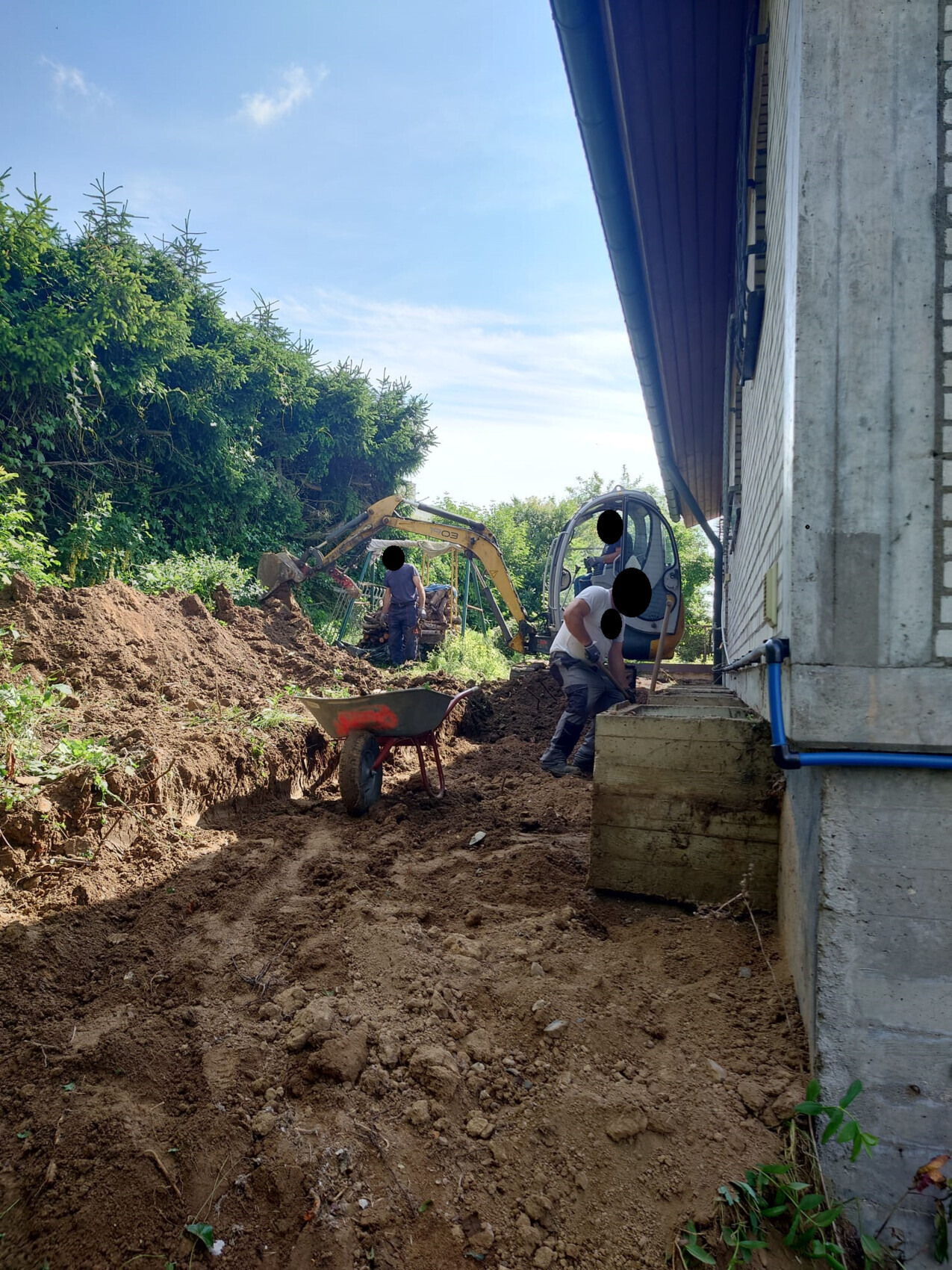 Baustelle am Haus: Bagger, Arbeiter und Schubkarre beim Aushub des Fundaments.