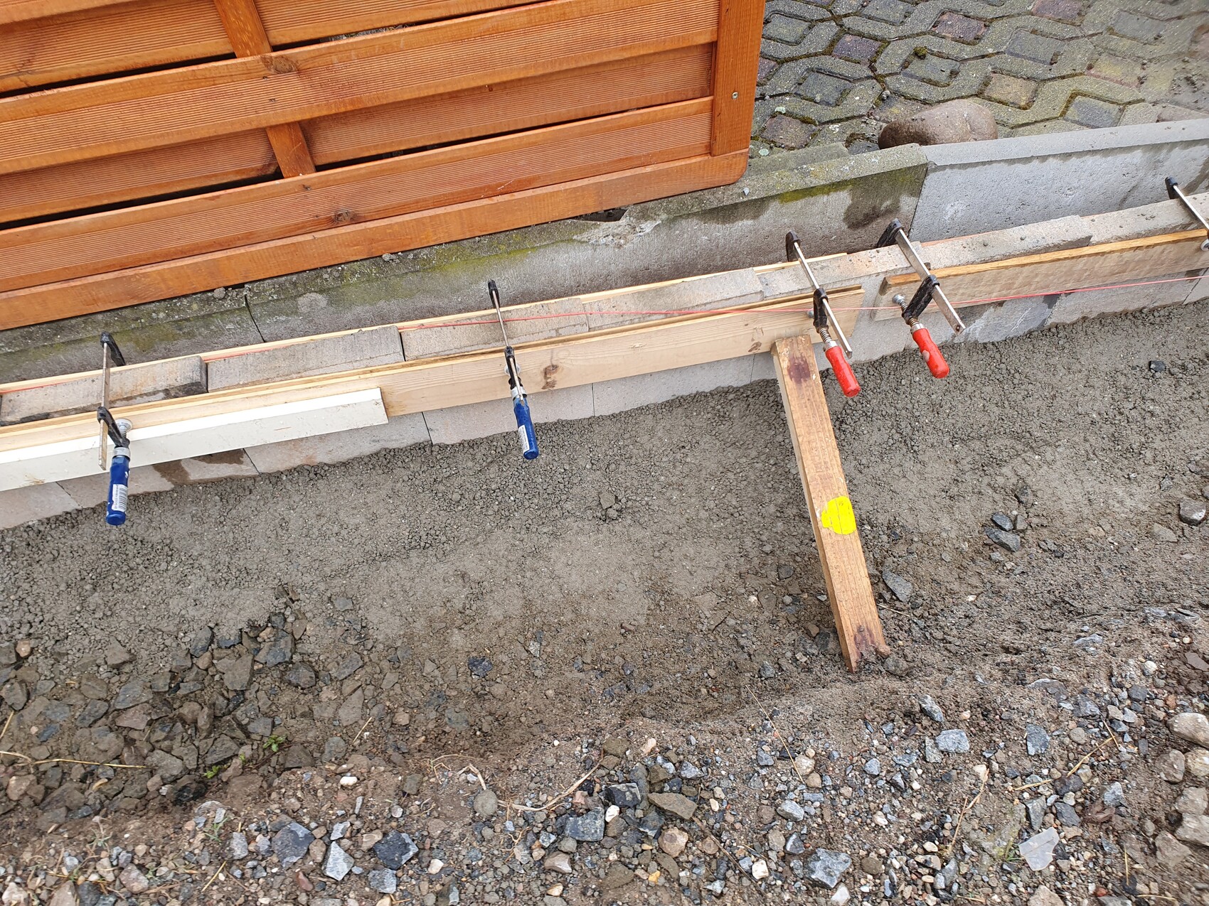 Baustelle: Holzformen mit Zwingen am Fundament, Kiesboden und Schotter.