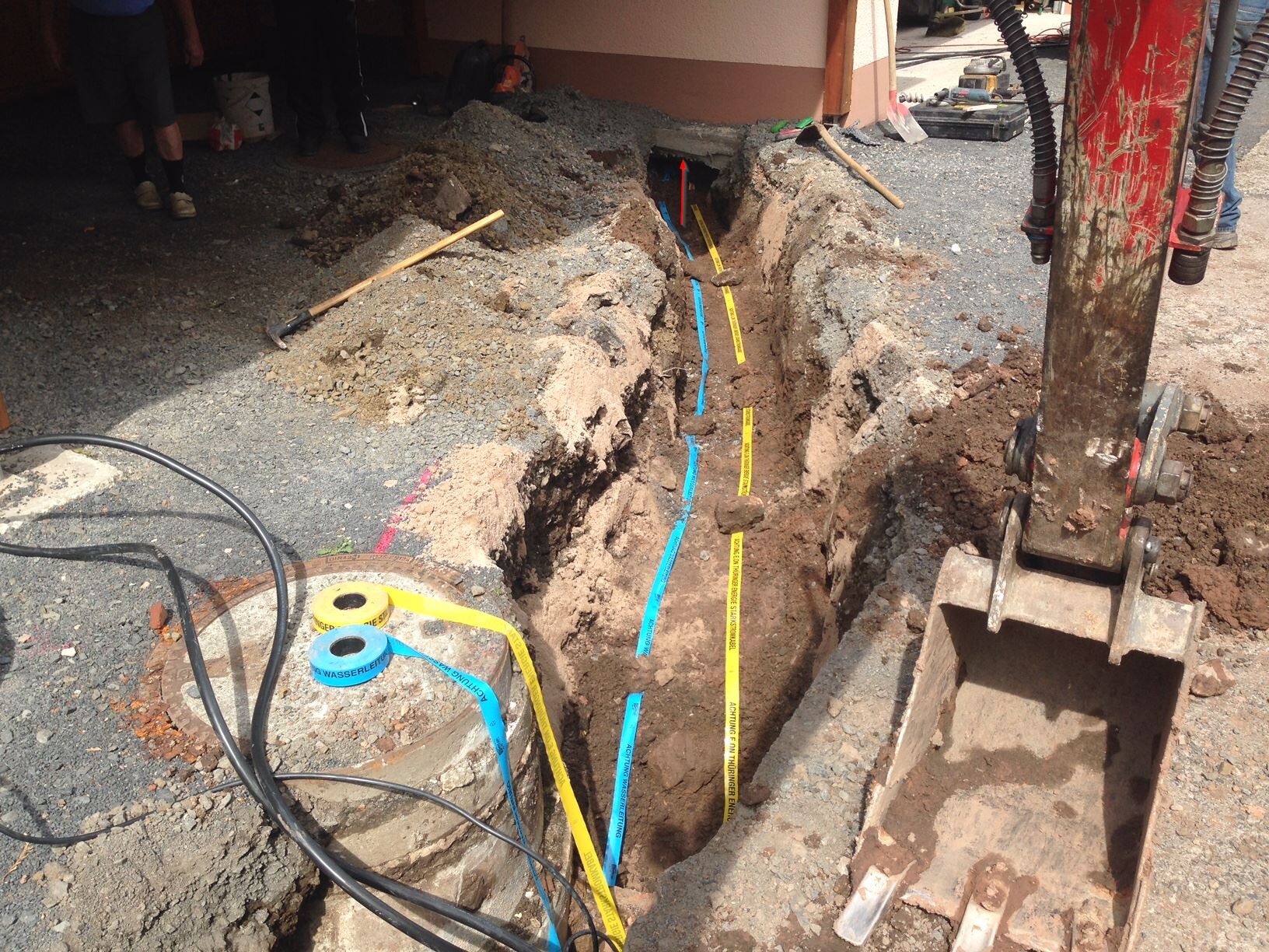 Ausgehobene Baugrube mit Rohren, Markierungen und Baumaschinen auf Baustelle