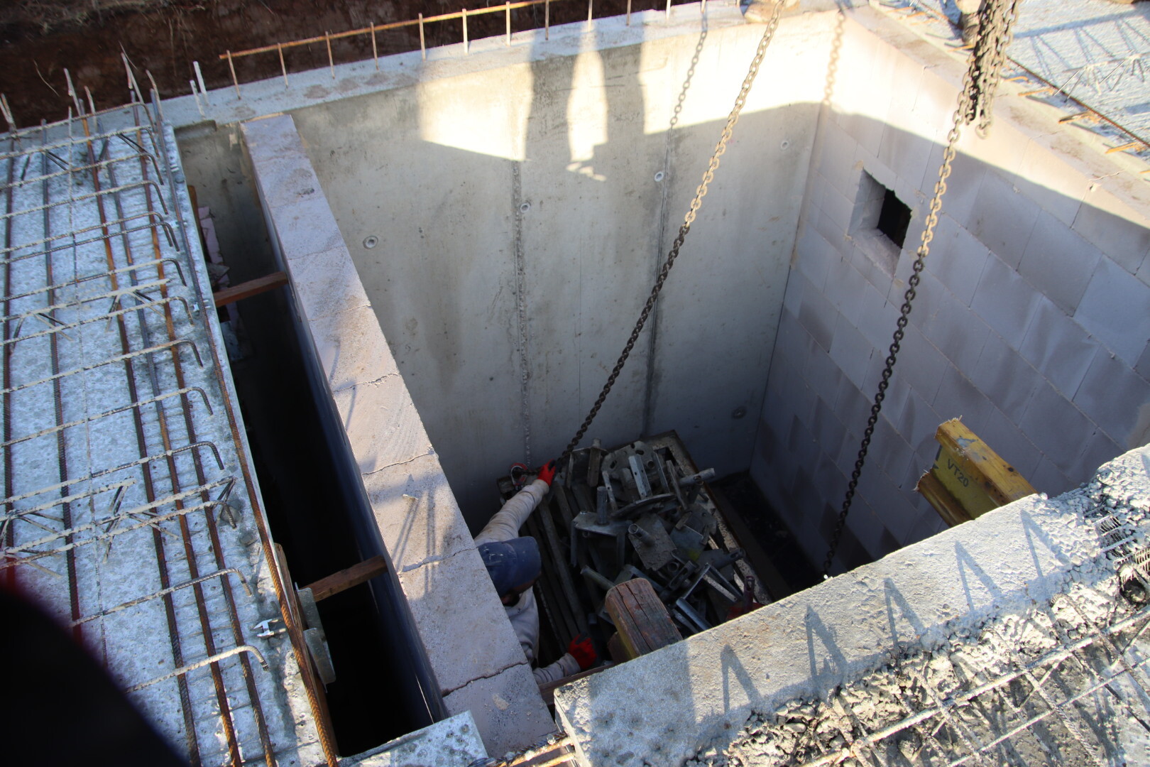Baugrube mit Betonschacht, Ketten, Schutt und Werkzeug; Arbeiter mit rotem Handschuh