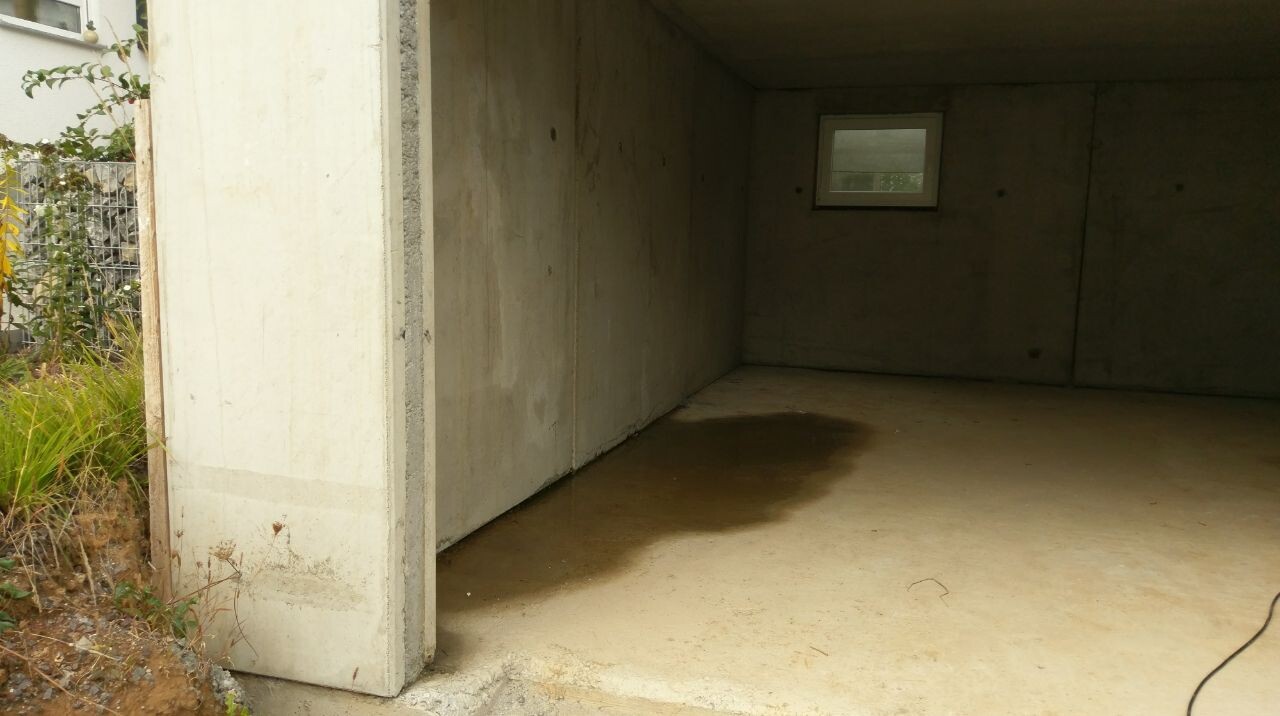 Leere Betongarage mit kleinem Fenster und feuchtem Boden