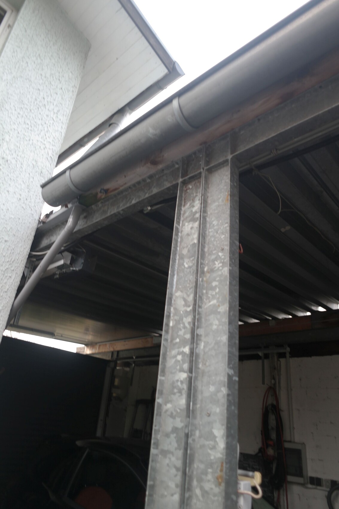 Sicht auf eine Garage mit Stahlträgern, Regenrinne und Rohren.