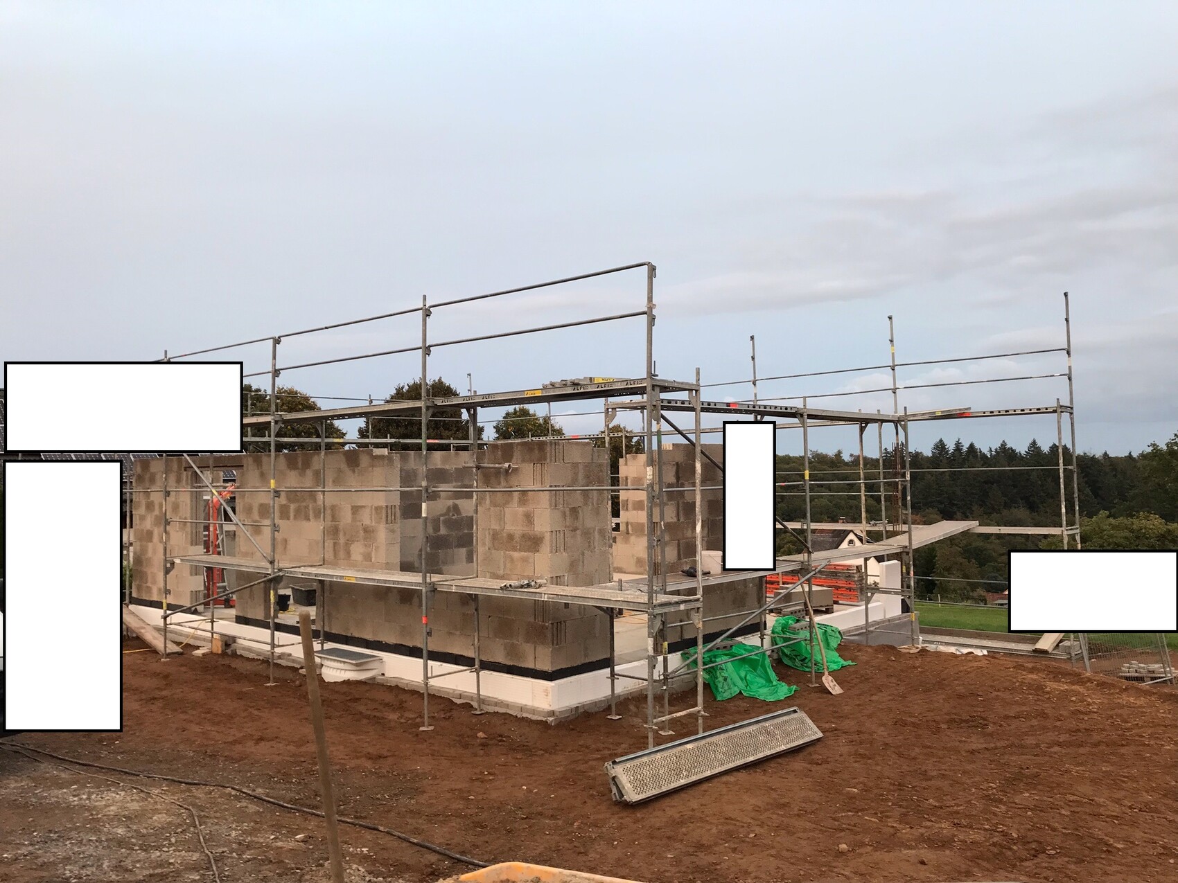 Baugerüst um ein unfertiges Haus aus Betonblöcken auf einer Baustelle.