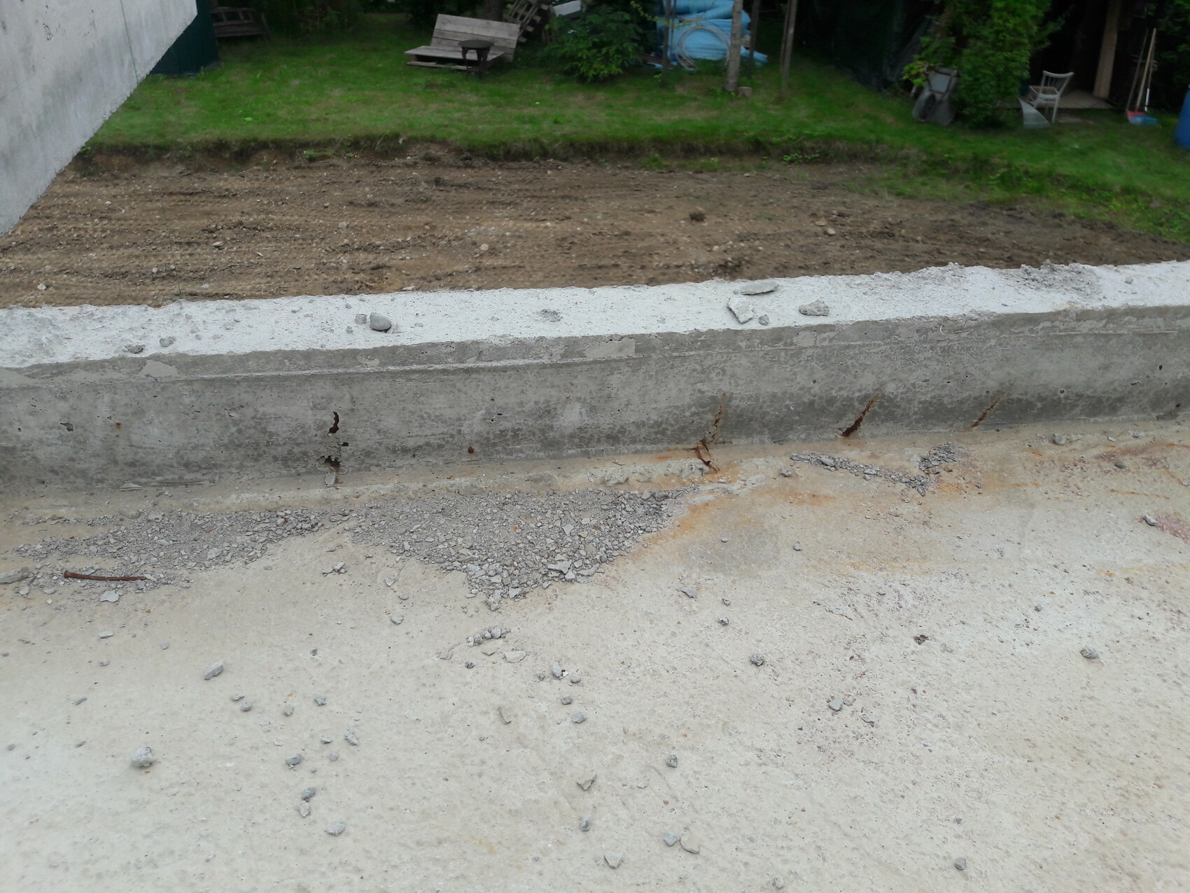 Betonfundament-Kante im Baugelände mit Erdreich, Kies und rostiger Bewehrung