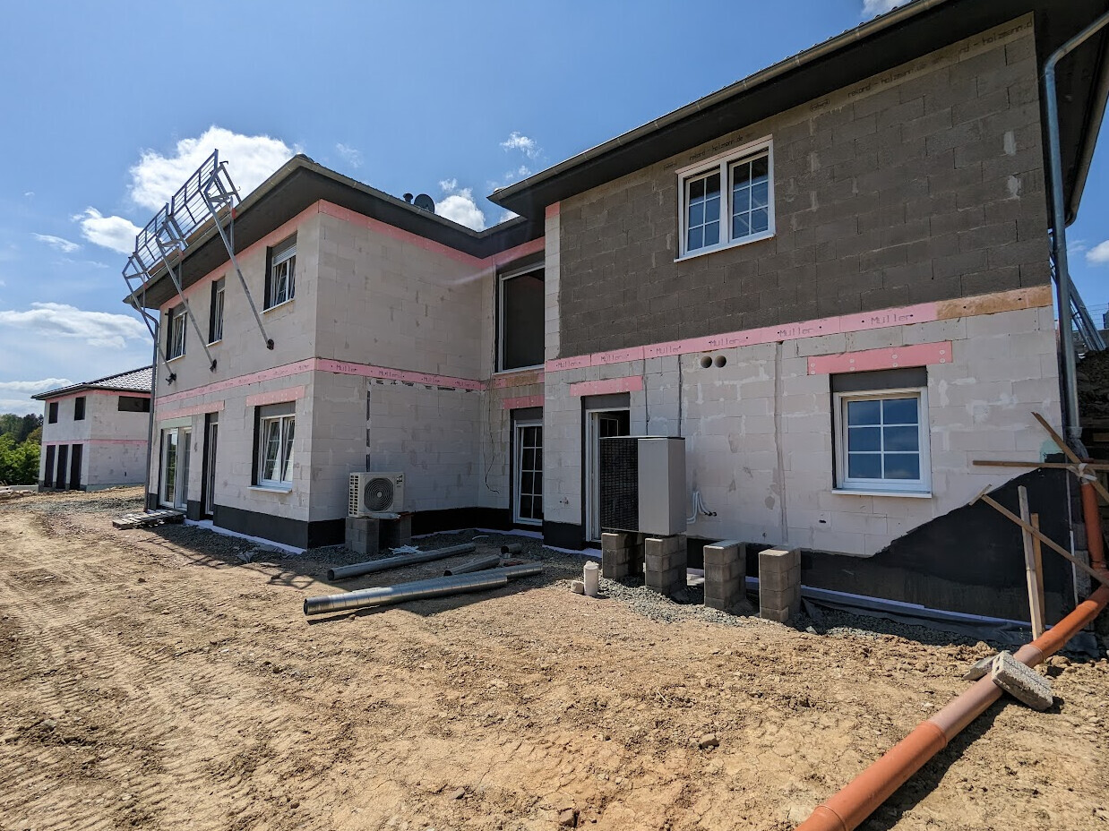 Außenansicht eines Rohbauhauses im Bau mit Fenstern und Baumaterialien