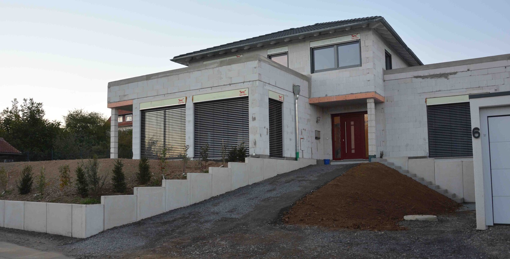 Unter Bau befindliches Haus mit Betonblöcken, Rollladenfenstern und Bauzufahrt.