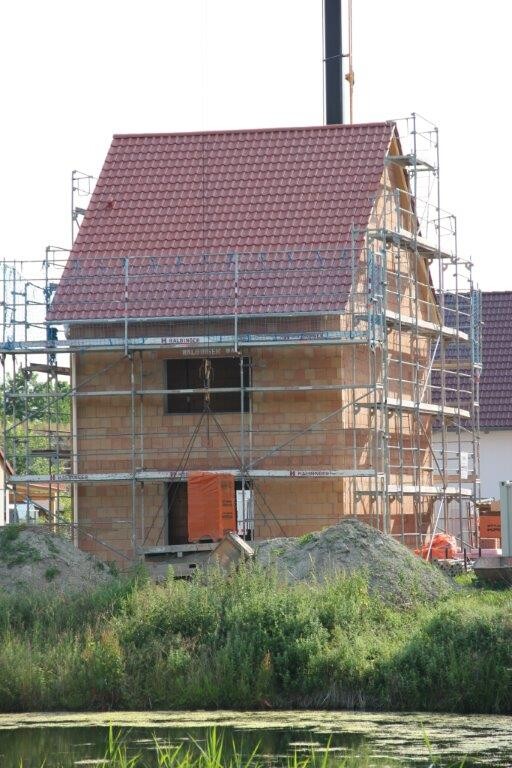 Haus im Rohbau mit Gerüsten, Ziegelmauerwerk und rotem Dachziegel