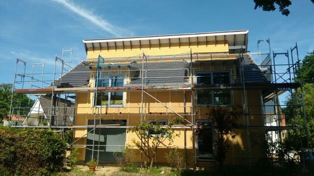 Zweigeschossiges Haus mit Gerüst, gelbe Fassade, Bauarbeiten im Freien, blauer Himmel.