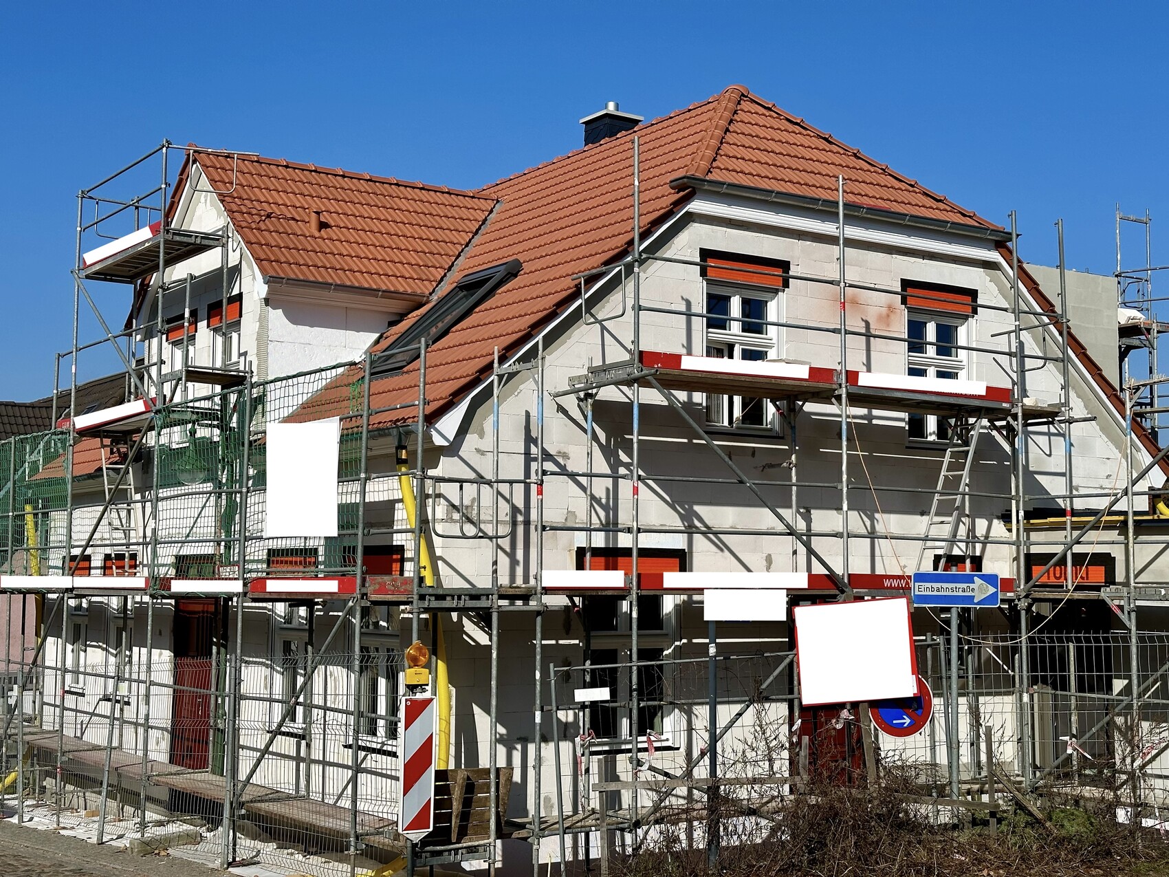 Unter Baugerüst stehendes Einfamilienhaus mit rotem Ziegeldach und Baugerüst