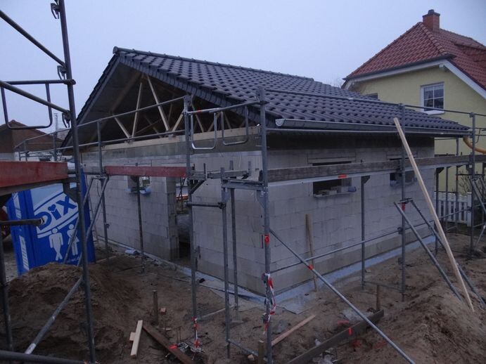 Rohbau eines Hauses mit Gerüst, Dachkonstruktion und Baugerüsten auf Baustelle