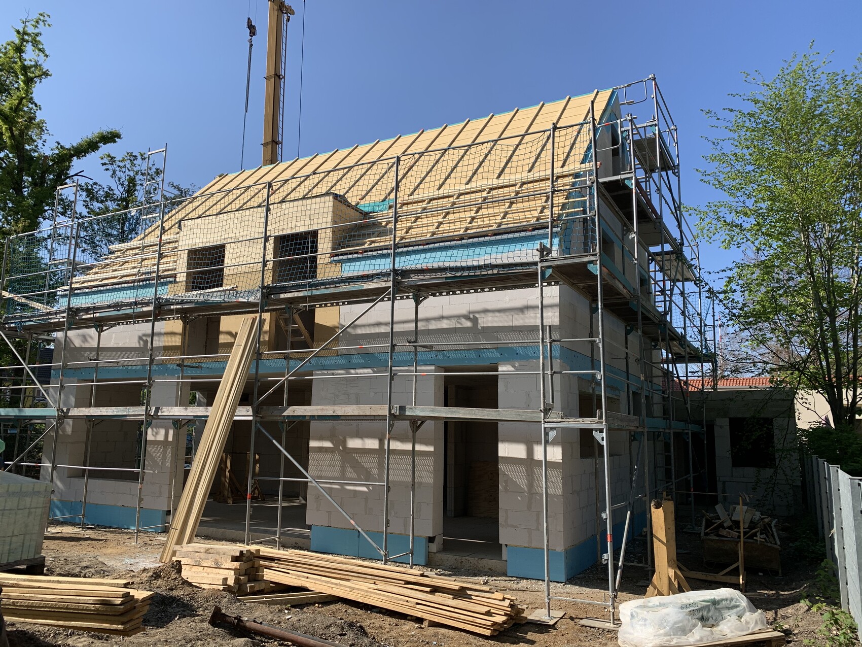 Neubau-Baustelle mit Geruest, Dachstuhlrahmen und Bauholz auf dem Hof.