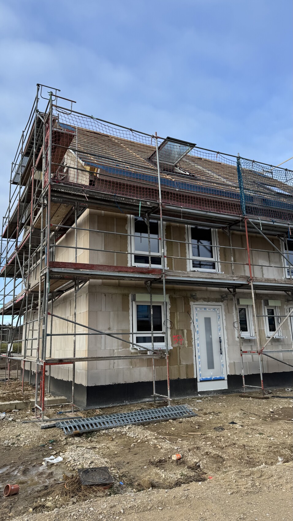 Mehrstöckiges Haus mit Gerüst umgeben; Bauarbeiten, Fenster, Tür und Bauabfall vor der Baustelle.