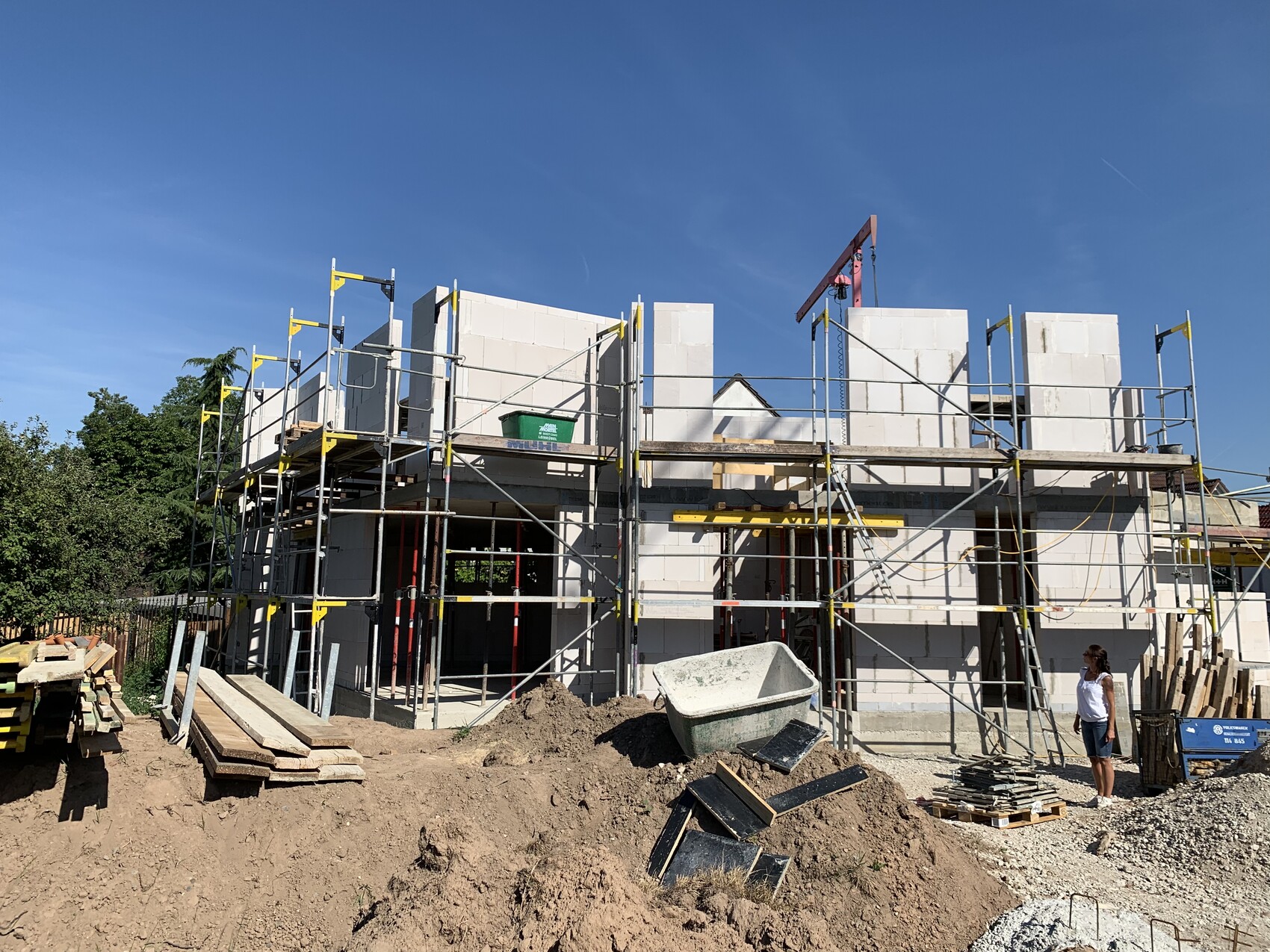 Baustelle mit Gerüst um ein Fertigbau-Haus aus Betonblöcken; eine Person steht rechts daneben.