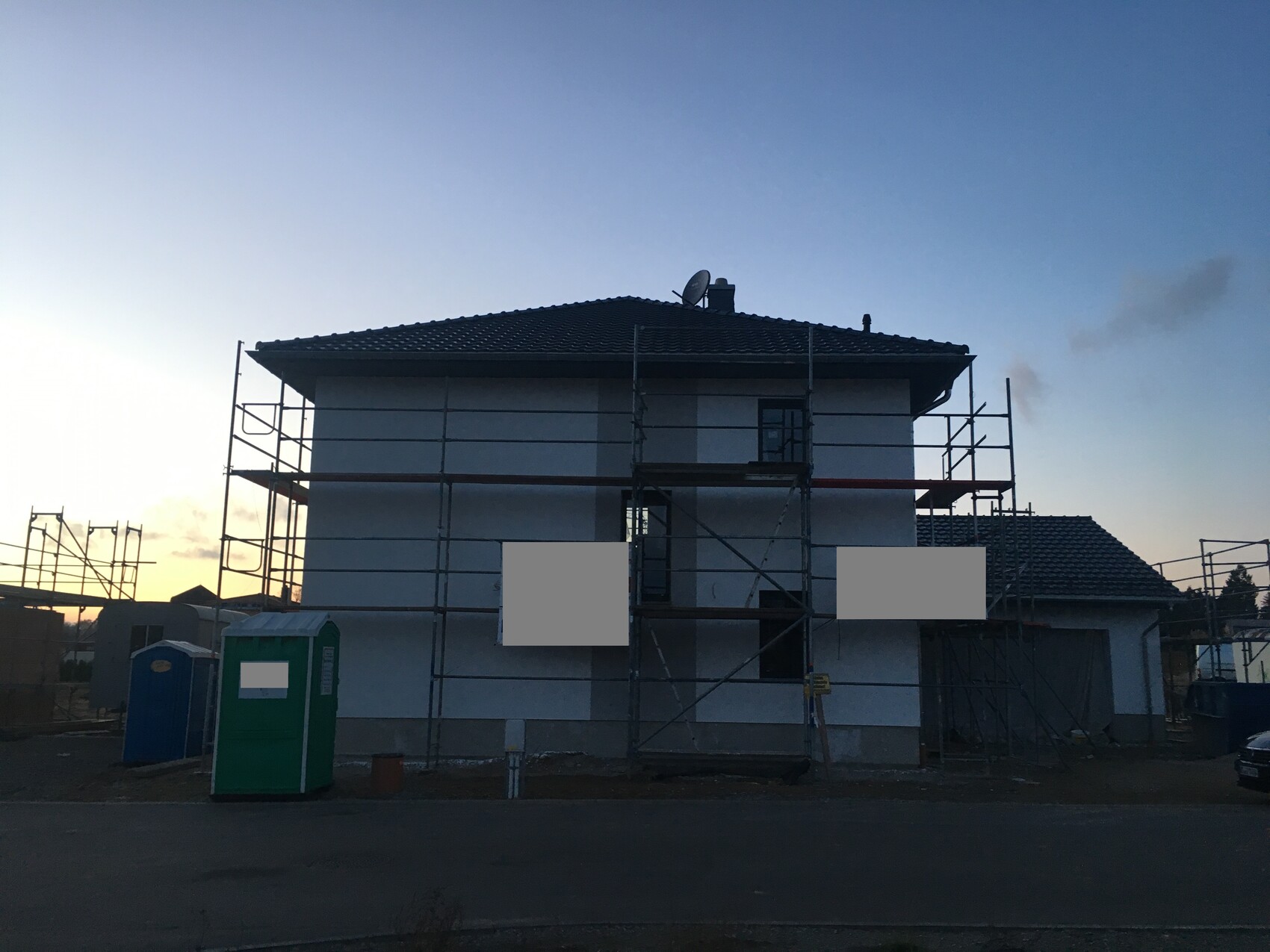 Zweistöckiges Haus im Bau mit Gerüsten und Satellitenschüssel bei Abenddämmerung.