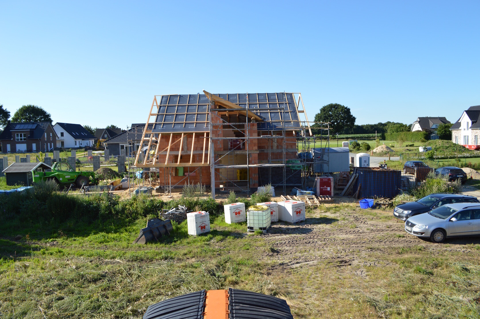 Rohbau eines Einfamilienhauses mit Holzrahmen und Gerüst auf einer Baustelle.