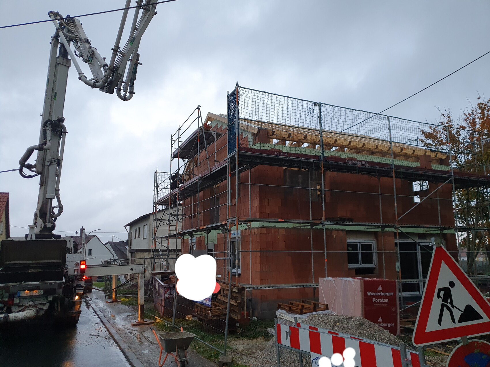 Baustelle: rotes Backsteinhaus im Rohbau mit Gerüst, Absperrungen und Warnschild
