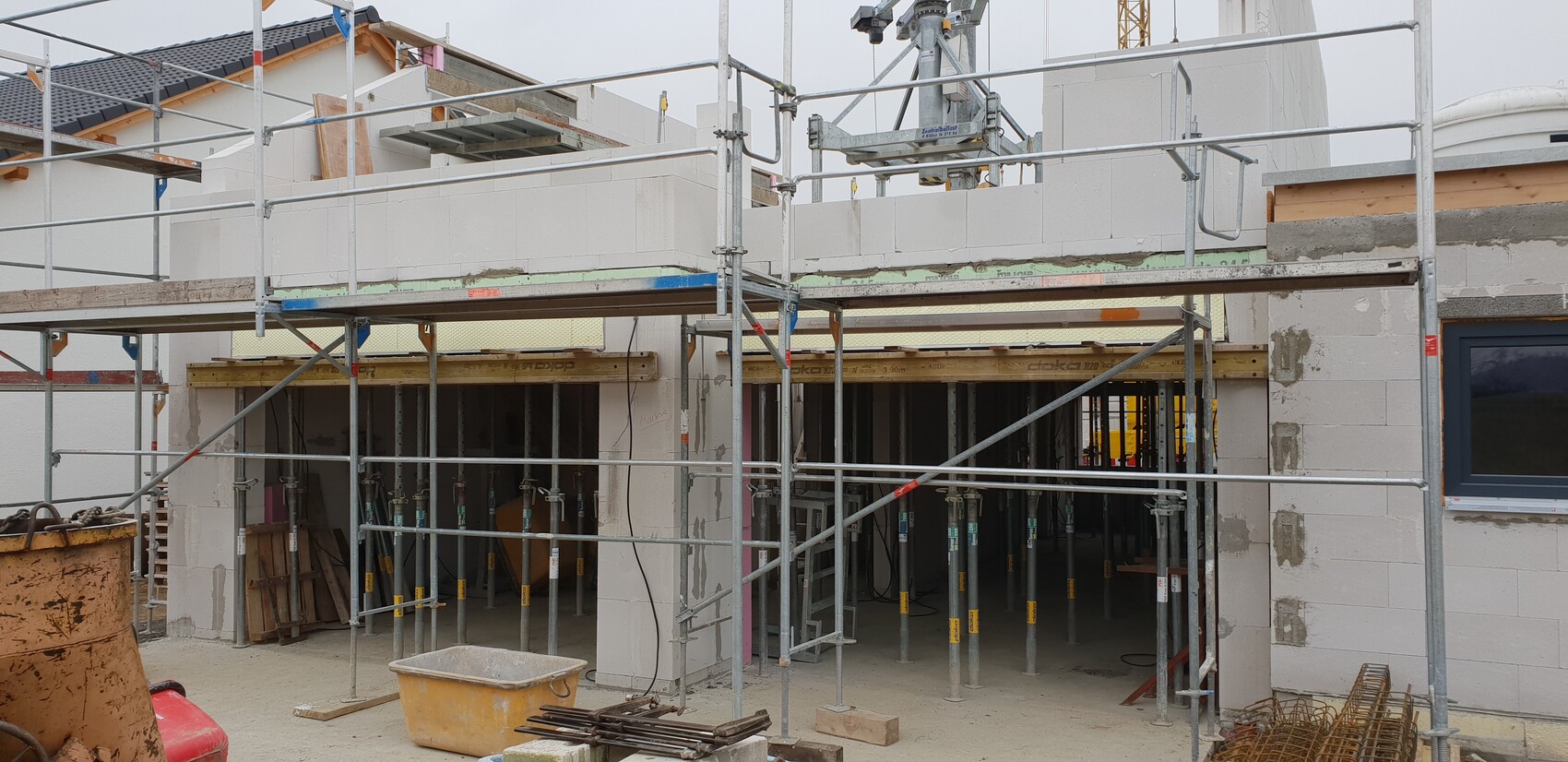 Baustelle mit Gerüst um Rohbau aus Betonblöcken, offener Innenbereich, Materialien im Vordergrund