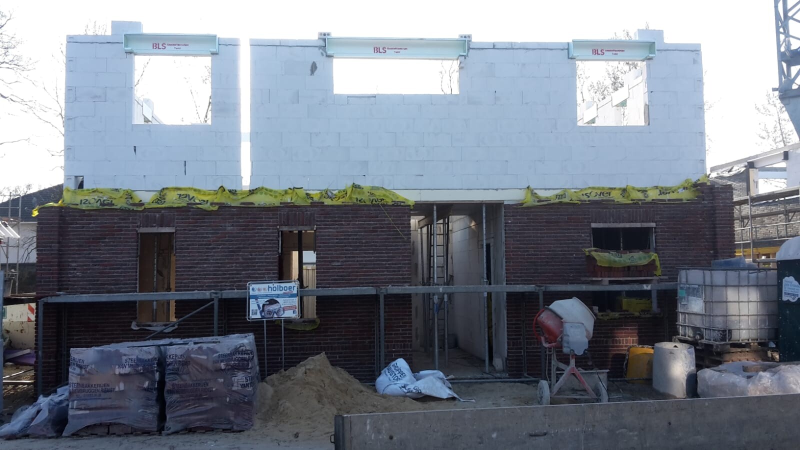 Zweistöckiger Rohbau mit Backsteinunterbau und weißem Obergeschoss auf Baustelle