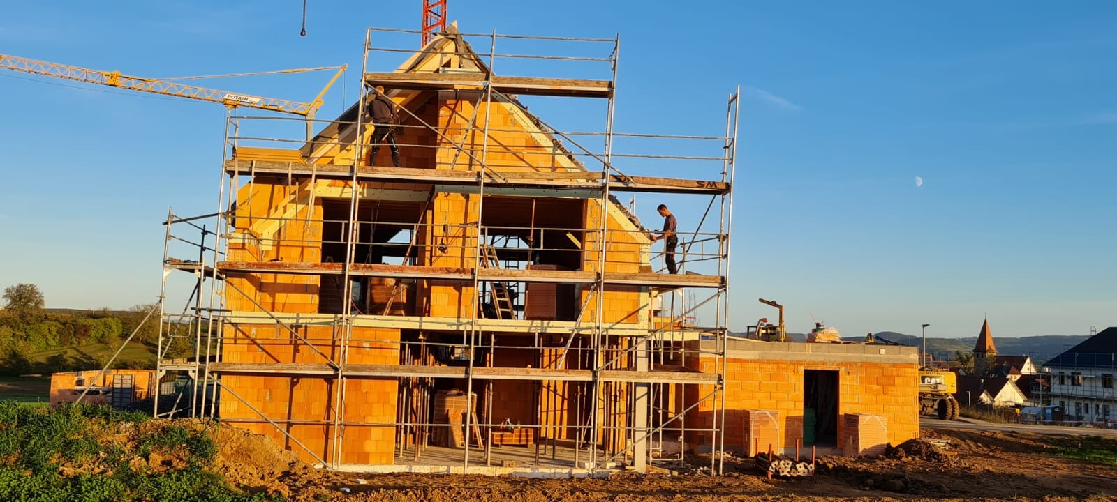 Rohbau eines gemauerten Hauses mit Gerüst und Arbeiter auf der Baustelle.