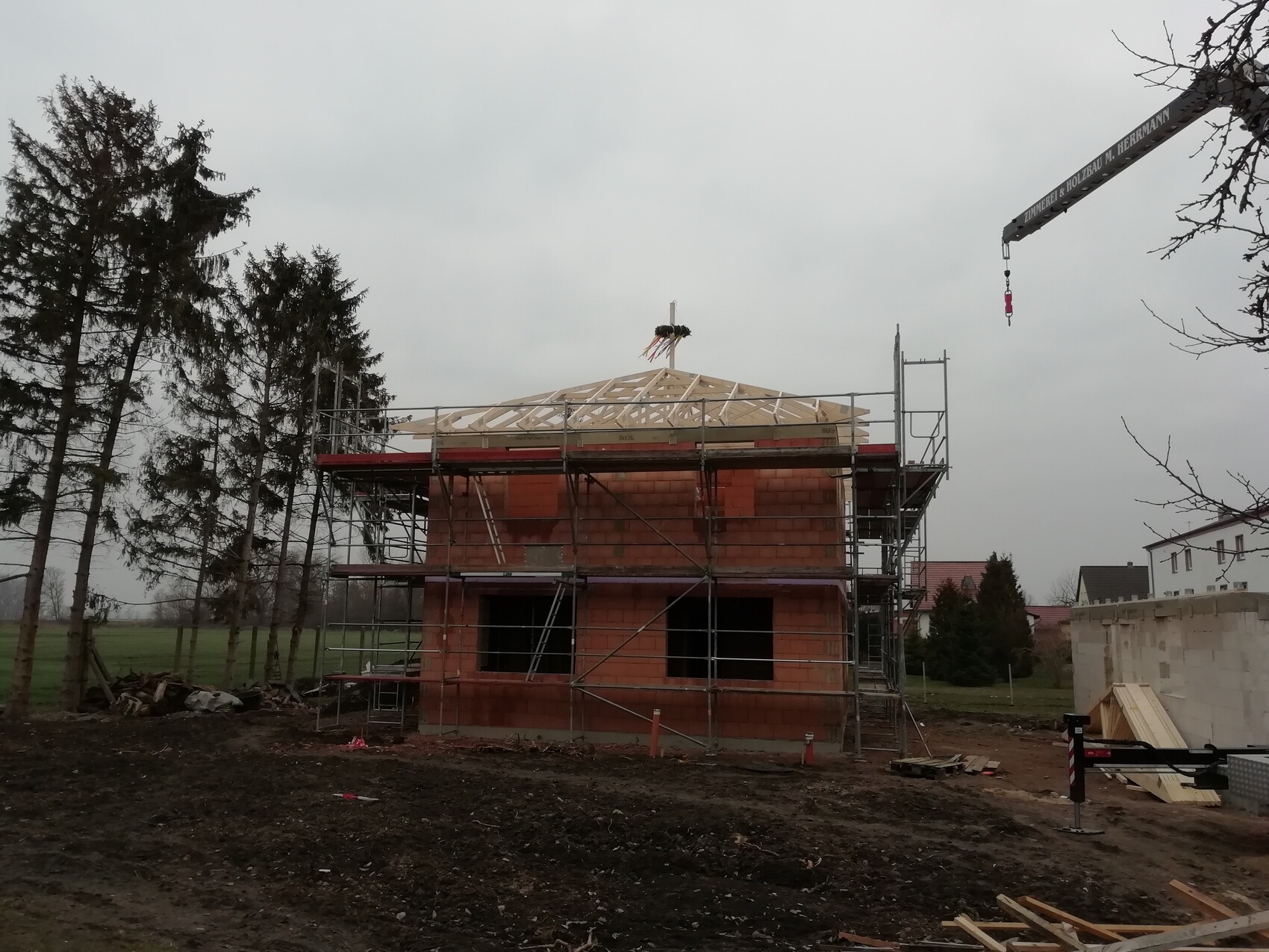 Rohbau eines zweigeschossigen roten Ziegelhauses mit Holz-Dachstuhl und Gerüst, Baukran rechts.