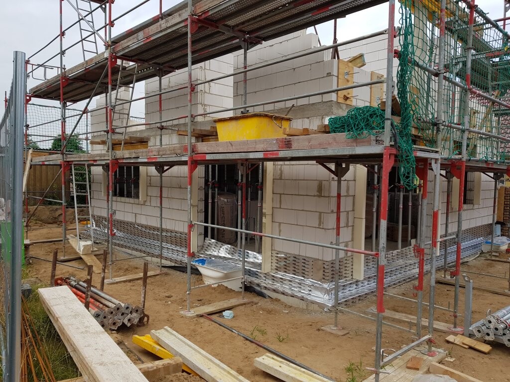 Neubau-Baustelle mit Gerüst, Mauerwerk-Blöcken und Bau-materialien rund ums Gebäude