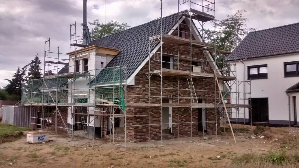 Hausbau im Rohbau mit Gerüst, Mauerwerk und Dachkonstruktion am Bauplatz