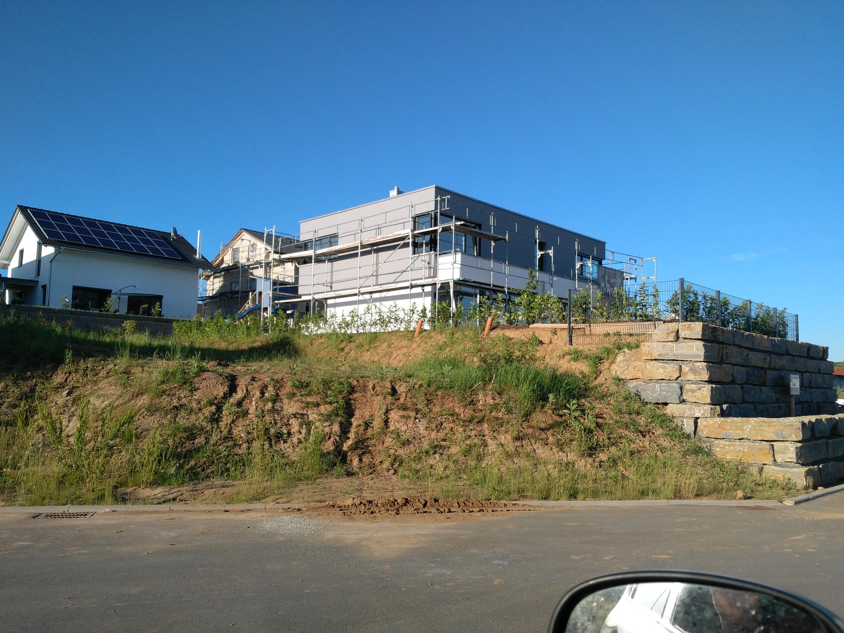 Bau eines modernen Hauses auf einem Hügel mit Gerüsten; links ein Haus mit Solaranlagen.
